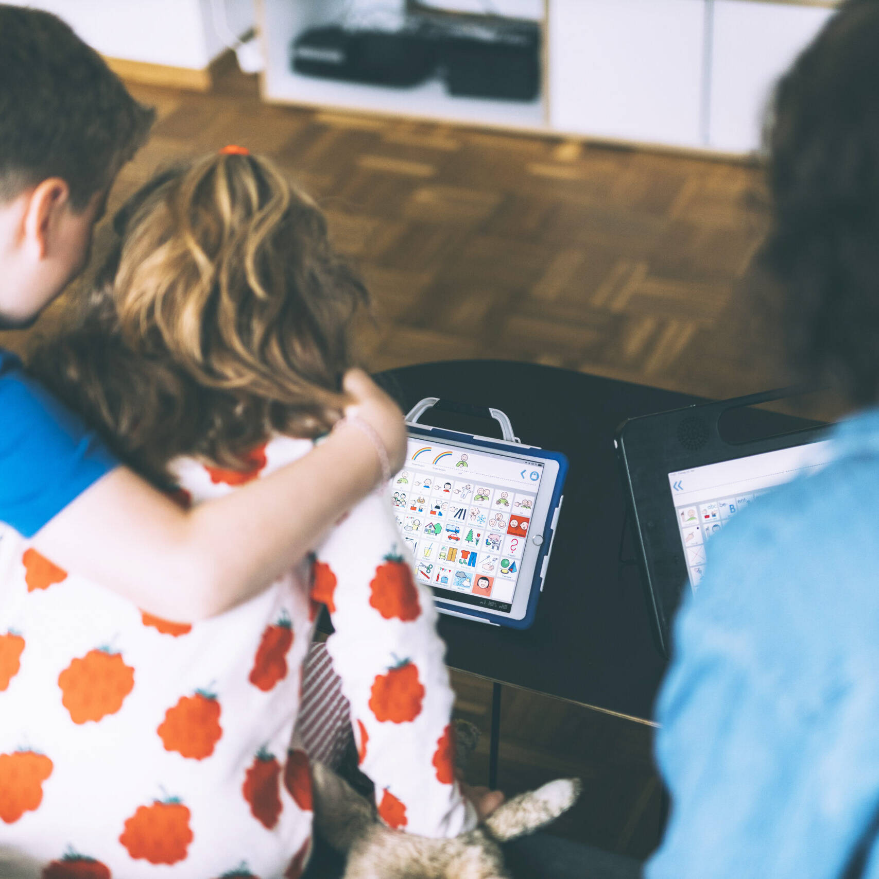 Zwei Kinder nehmen sich in den Arm und schauen auf ein Tablet mit Software zur Unterstützten Kommunikation